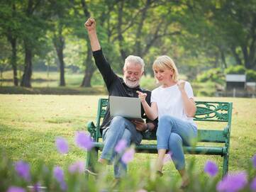 Mann und Frau sitzen im Park auf einer Bank und schauen gemeinsam auf einen Laptop