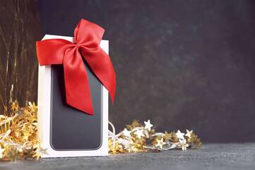 Smartphone-Verpackung mit einer roten Schleife steht vor goldener Sternen-Lichterkette