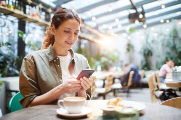 Frau sitzt in Café und schaut lächelnd auf Smartphone