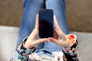 Frau sitzt auf Sofa mit Smartphone in beiden Händen
