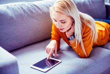 Frau liegend auf einem Sofa am Tablet