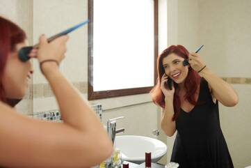 Frau schminkt sich vor einem großen Spiegel, während sie telefoniert