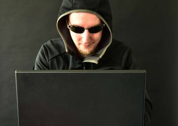 Person mit Kapuze und Sonnenbrille vor einem Laptop