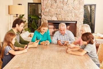 6 Personen sitzen an einem Esstisch und schauen alle auf ihr Smartphone