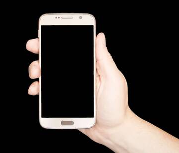 Eine Hand hält rosé farbenes Smartphone mit dem Bildschirm nach vorne gerichtet. Der Bildschirm ist schwarz.