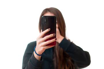 Frau hält Smartphone mit ausgestrecktem Arm vor Gesicht