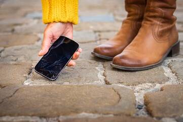 Smartphone mit kaputtem Bildschrim wird von einer Person vom Boden aufgehoben