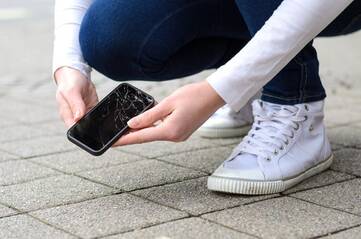 Person hebt Smartphone mit gebrochenem Display vom Boden hoch