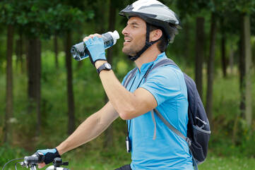 Radfahrer mit Helm trinkt aus Trinkflasche