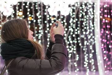 Frau hält Smartphone in der Hand. Im Hintergrund sind viele Lichter zu sehen.