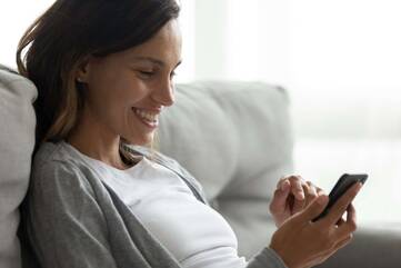 Frau hält Smartphone in den Händen und schaut entspannt lächelnd auf ds Display