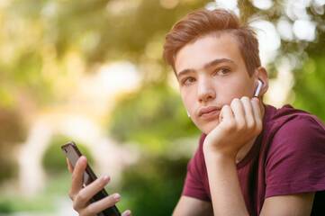 Jugendlicher sitzt draußen am Handy mit AirPods in den Ohren