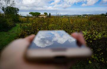 Hand hält draußen Smartphone in der Hand, sodass sich die Wolken darin spiegeln