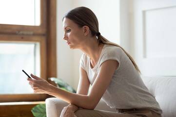 eine Frau sitzt auf einem Sofa und schaut auf ihr Smartphone
