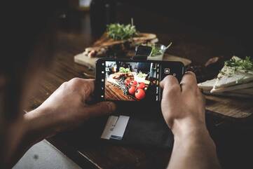 Person macht Photo mit Smartphone von Gemüse auf einem Tisch