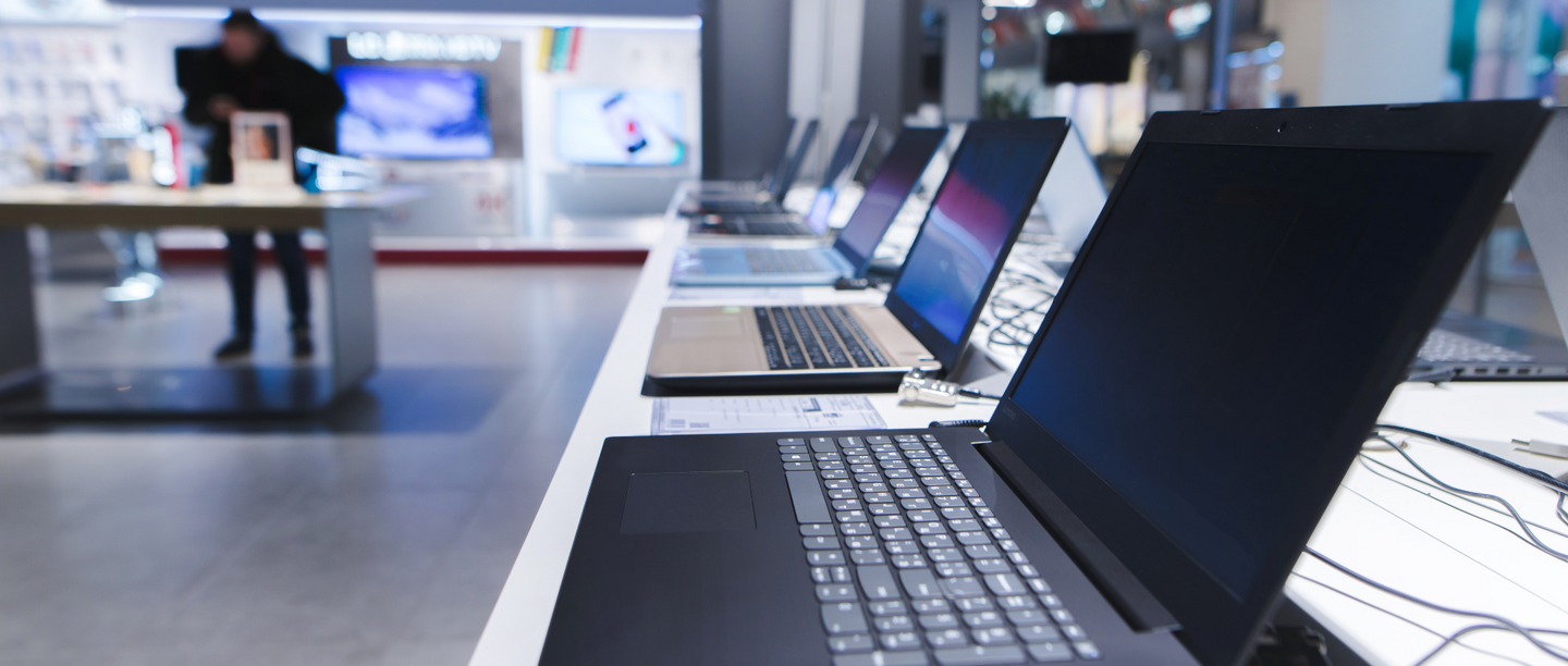 Mehrere Laptops stehen aufgereiht auf einem langen Tresen in einem Elektronikgeschäft.