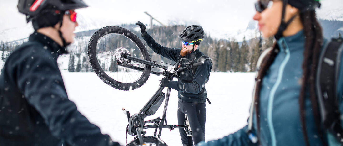 Mann in Winterlandschaft hält sein E-Bike aufrecht und betrachtet es