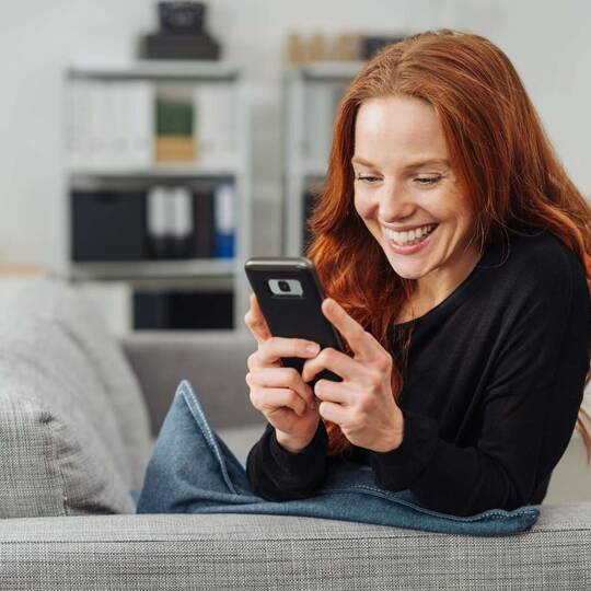 Frau schaut lächelnd auf Smartphone Display
