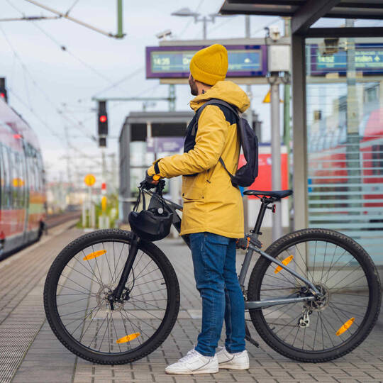 Mann in gelber Jacke wartet mit seinem Fahrrad auf den Zug