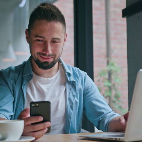 ein Mann sitzt mit Laptop und seinem Smartphone in einem Cafe