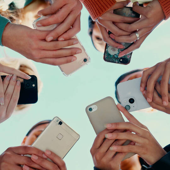 Mehrere Personen halten ihr Smartphone in der Hand und stehen dabei im Kreis. 