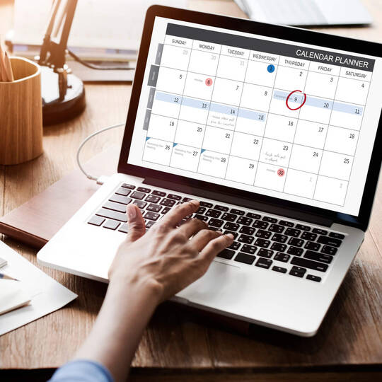 Eine Person sitzt am Laptop und schaut auf ihren Kalender.
