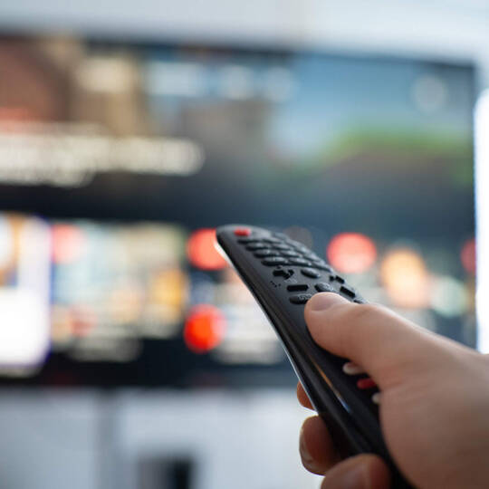 Eine Person hält eine Fernbedienung in Richtung des Fernsehers.