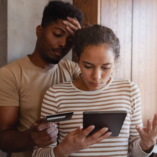 Ein Pärchen blickt besorgt und fassungslos auf ihr Endgerät während eines Bezahlvorgangs.