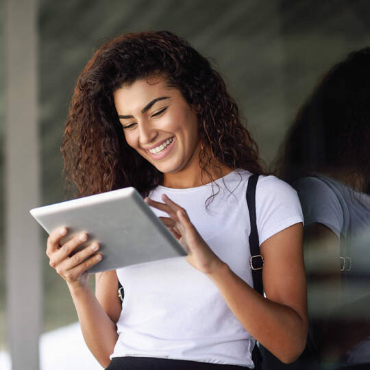 Eine Frau blickt auf ihr Tablet und lacht. 