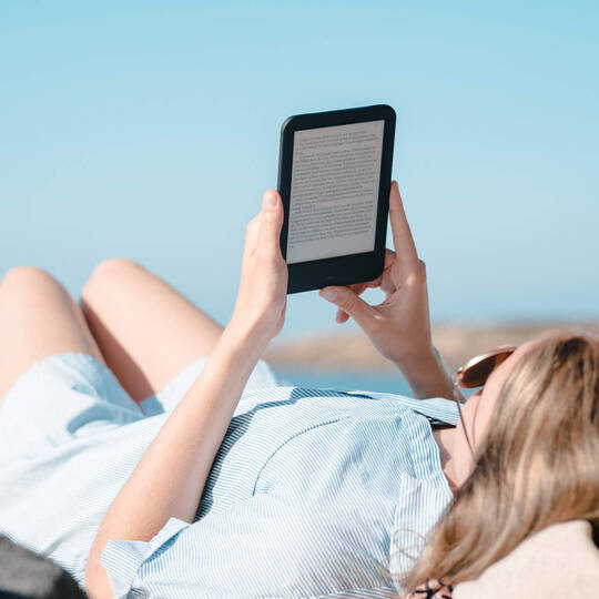 Eine Frau liegt am Strand und liest in einem E-Book-Reader.