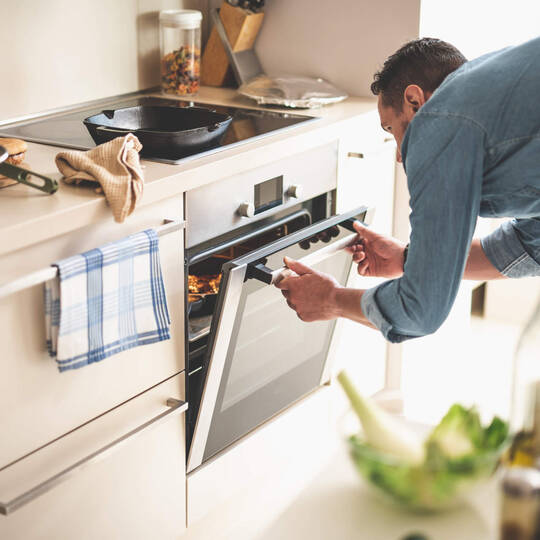 Ein Mann öffnet seinen Backofen in der Küche.