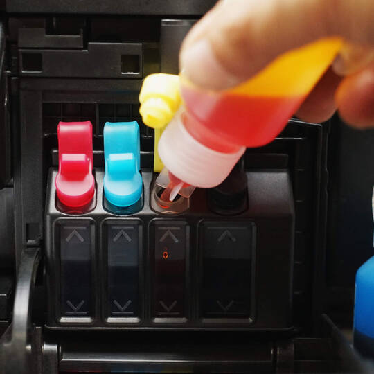 Eine Person füllt die Farbtanks im Drucker auf.