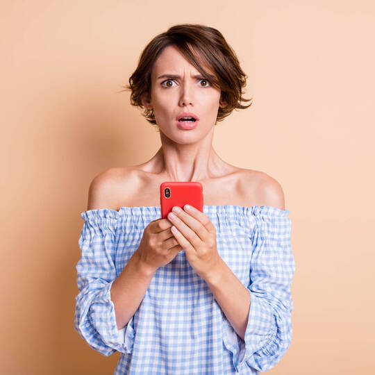 Eine Frau blickt verdutzt, während sie ihr Handy in der Hand hält.
