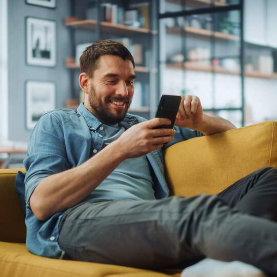 Ein Mann sitzt auf dem Sofa und schaut auf sein Smartphone.