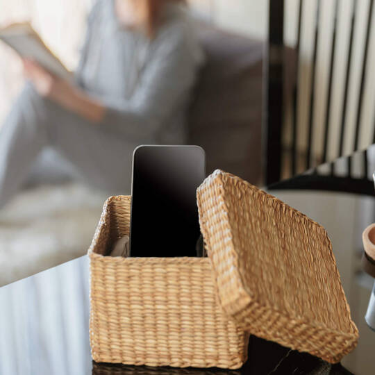 Eine Person sitzt auf dem Sofa, lässt das Handy links liegen und liest ein Buch.