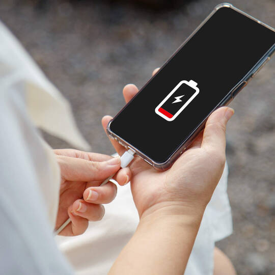 Eine Person hält ein leeres Smartphone in der Hand und steckt es ans Ladekabel.