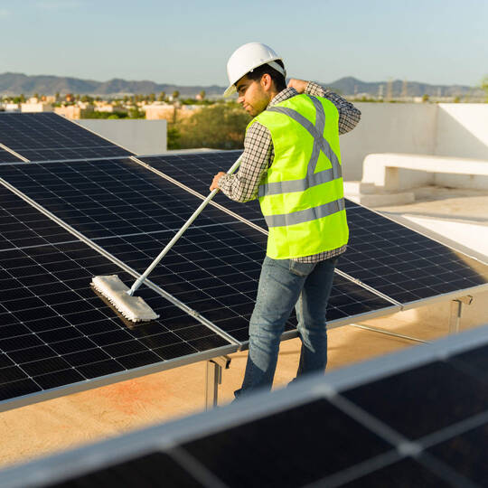 Ein Mann steht auf einem Dach und säubert eine PV-Anlage.
