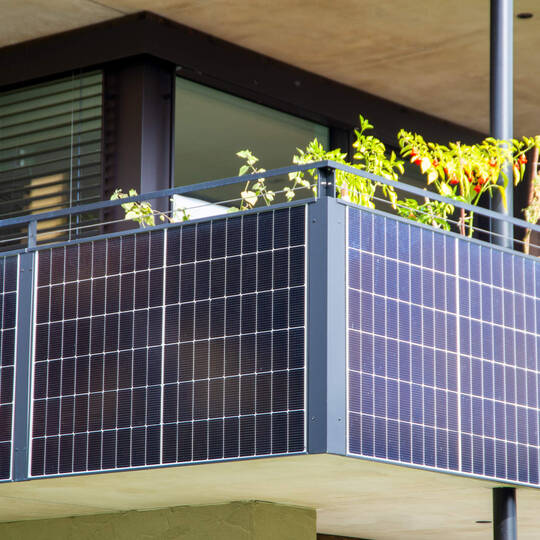 An einem Balkon sind mehrere Solarmodule installiert.