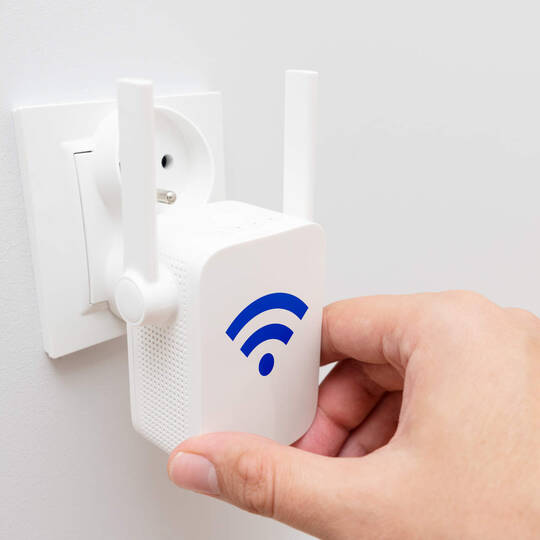 Eine Person steckt einen WLAN-Verstärker in die Steckdose. 