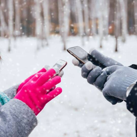 Zwei Personen an ihren Handys mit Handschuhen in einer Winterlandschaft