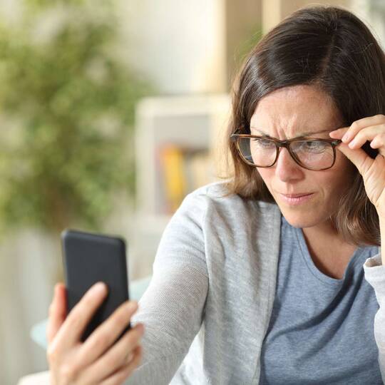 Eine Frau mit Brille schaut skeptisch auf ein Smartphone.