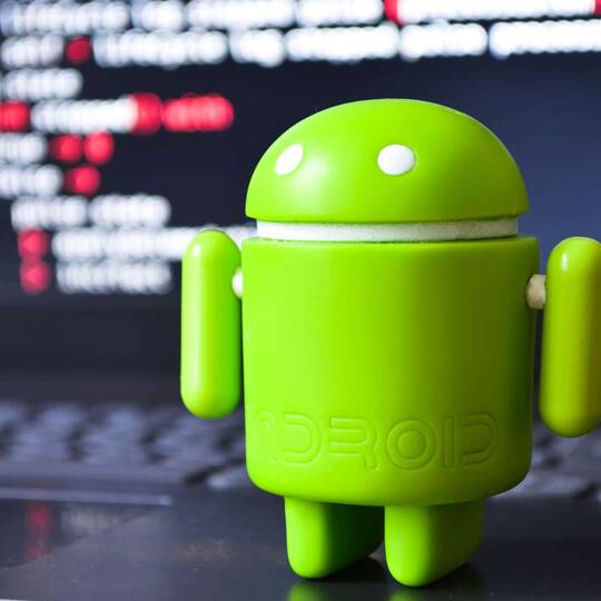 Plastisches Android Symbol steht vor Rechner mit angezeigter  Programmiersprache