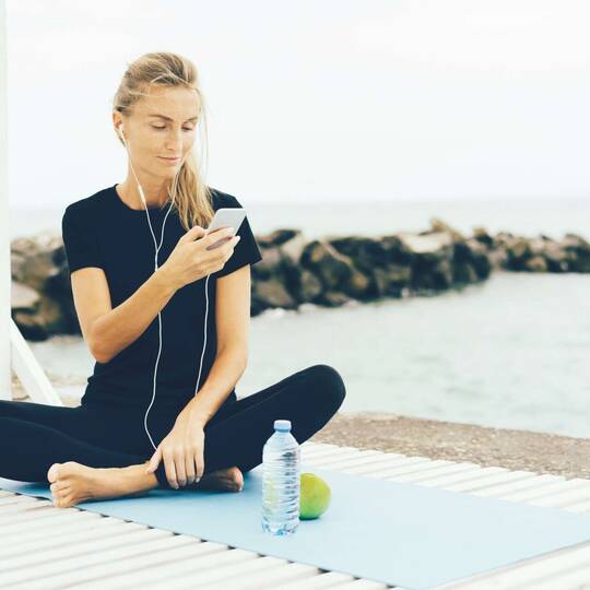 eine Frau sitzt auf einer YogaMatte mit deinem Smartphone in der Hand