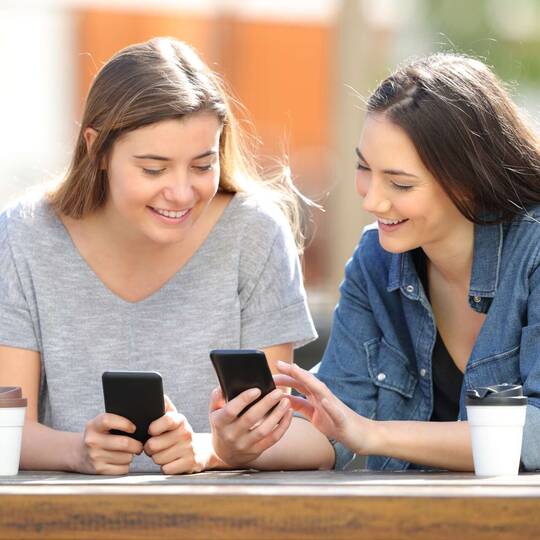 Zwei Frauen zeigen sich etwas auf ihren Smartphones beim Kaffee