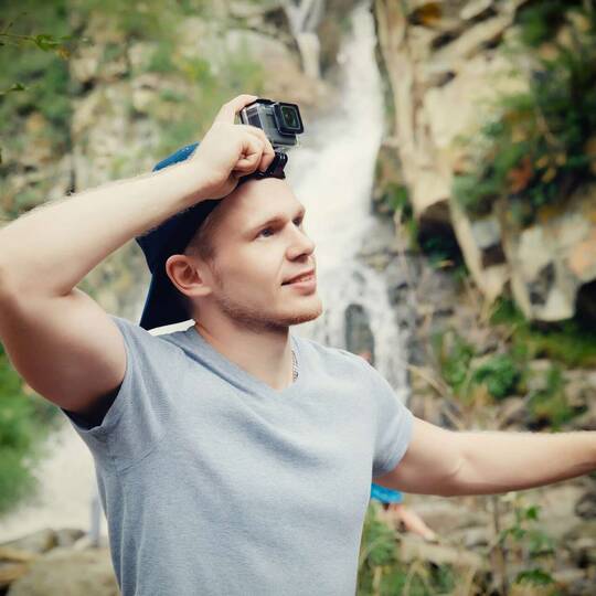Junger Mann mit Go pro auf Kopf vor Wasserfall