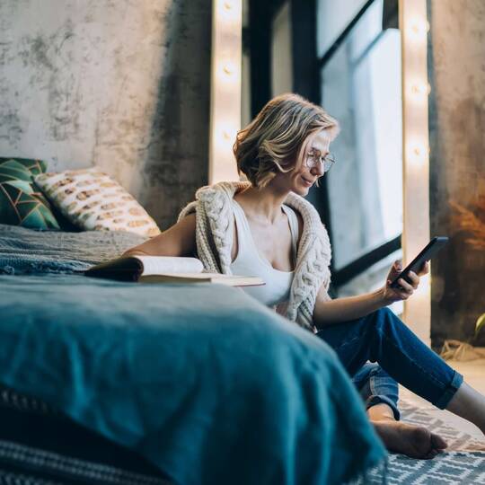 Frau lehnt an Bett und schaut auf Smartphone-Display
