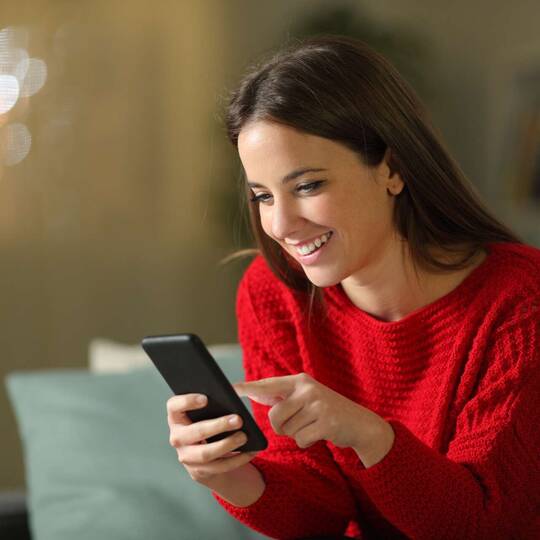 Frau im roten Pullover schaut lächelnd auf Smartphone