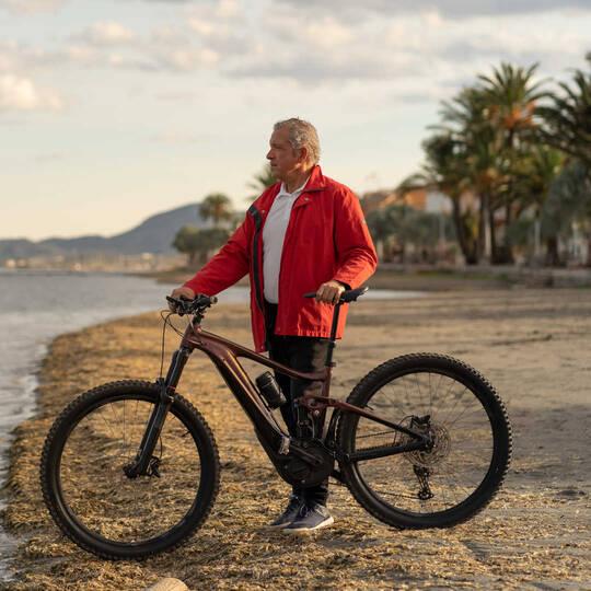 Mann steht mit Mountainnbike am Strand