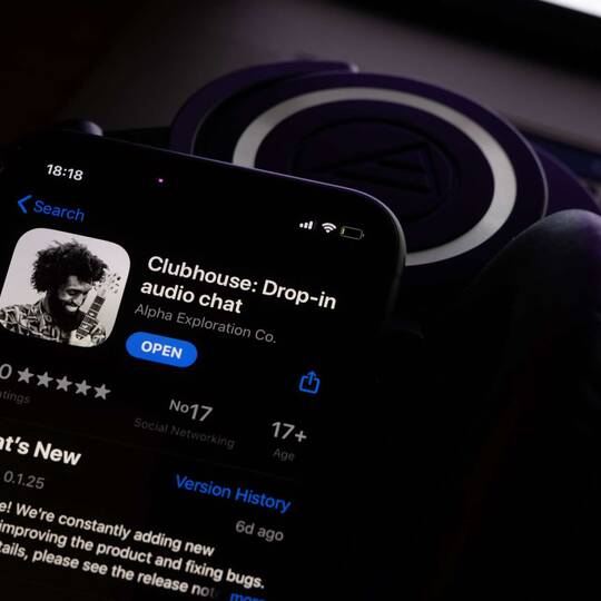 Smartphone mit Clubhouse App in App Store vor dunklem Hintergrund