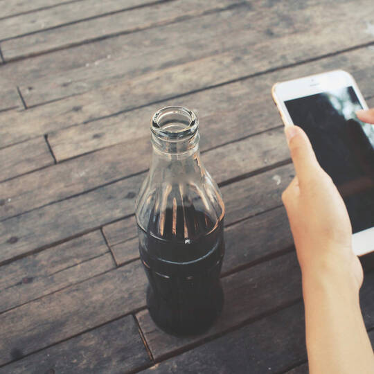 Handy in der Hand und daneben steht eine Cola